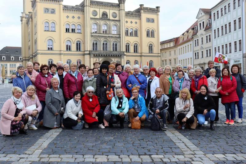 Seniorki i seniorzy pozujący do grupowego zdjęcia. W tle budynek zabytkowy miasta Zittau. Autor: Stowarzyszenie P-ZFST Pogranicze